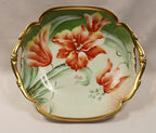 Decorative ceramic dish with floral design and gold handles on a plain background
