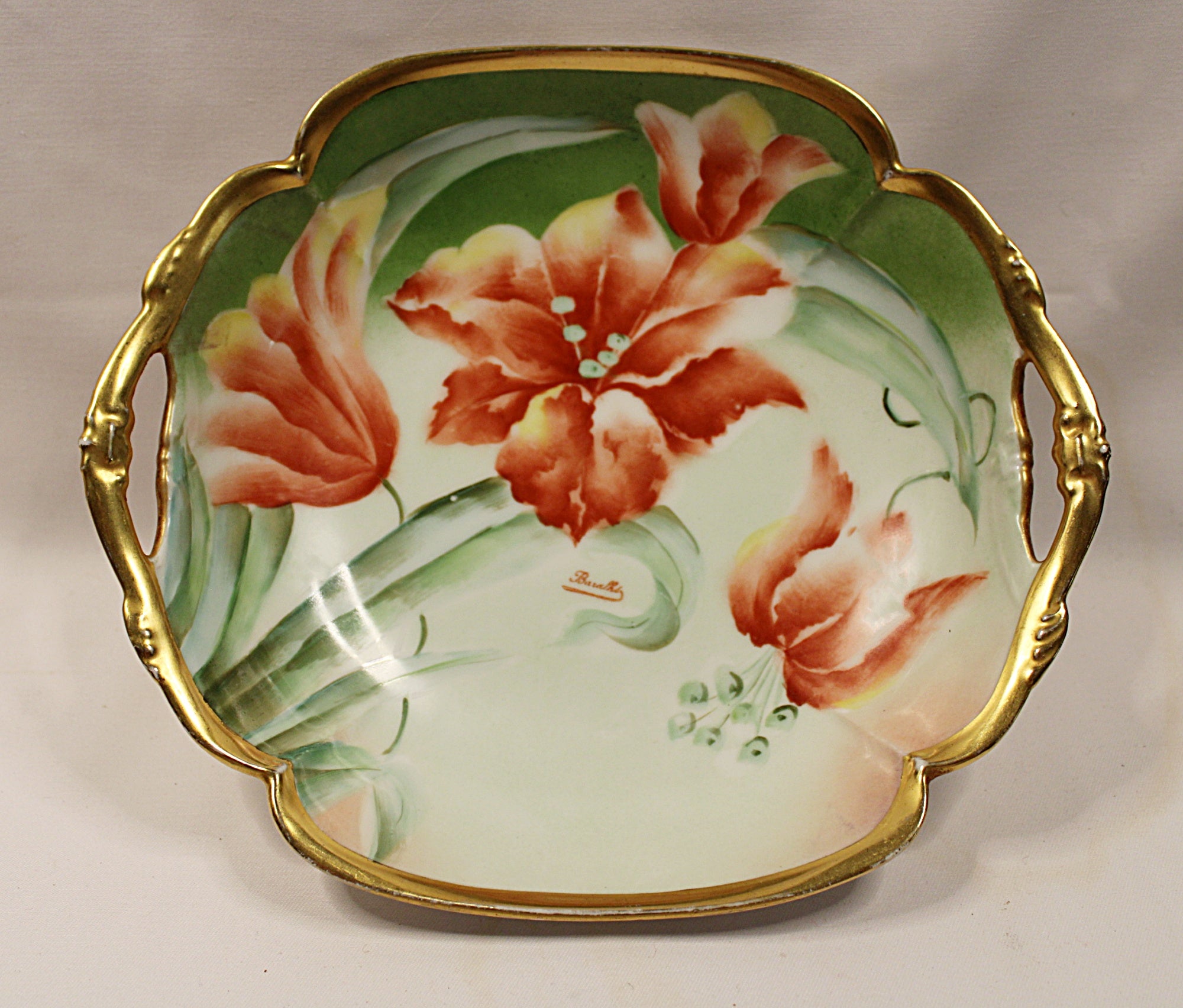 Decorative ceramic dish with floral design and gold handles on a plain background