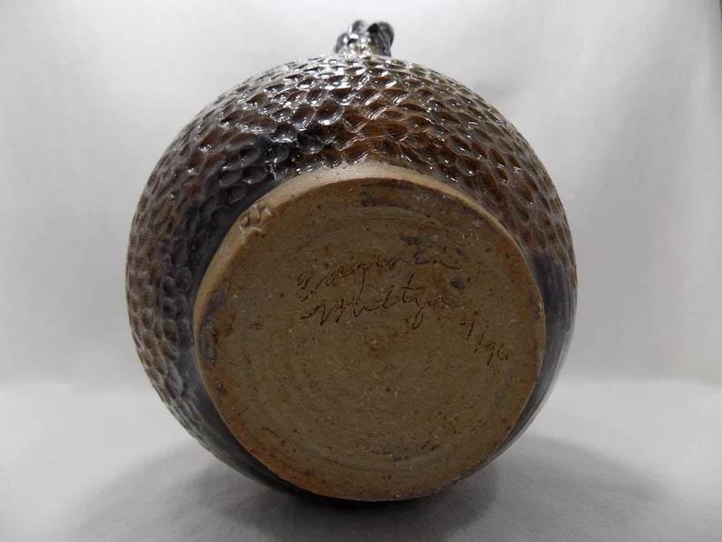 Ceramic jar with textured surface and visible signature on a white background