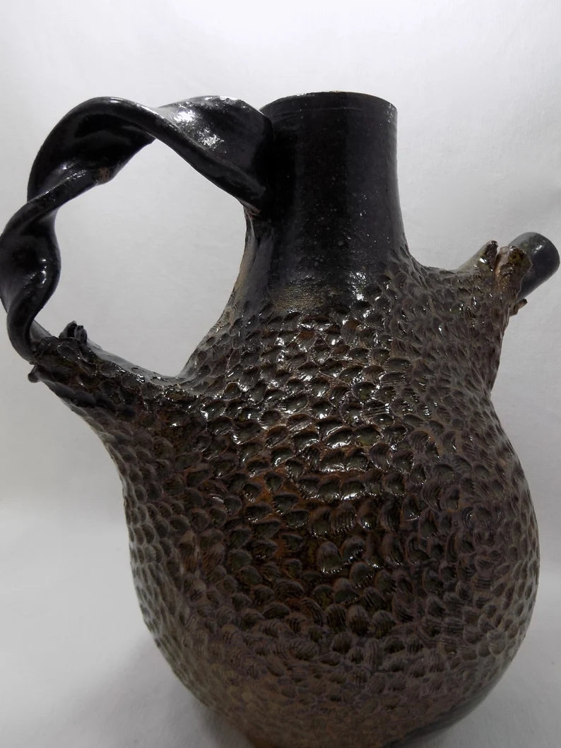 Textured black ceramic pitcher on a white background