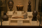 Collection of African art pieces in a glass display case with labels.