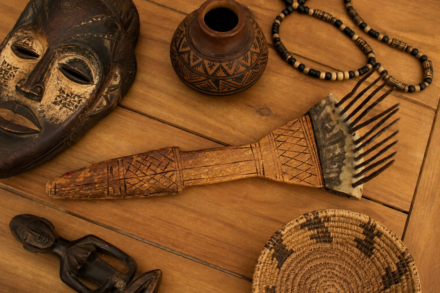 Collection of wooden artifacts including a mask, comb, and beads on a wooden surface.