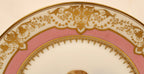 Decorative plate with gold intricate patterns on a pink background top rim