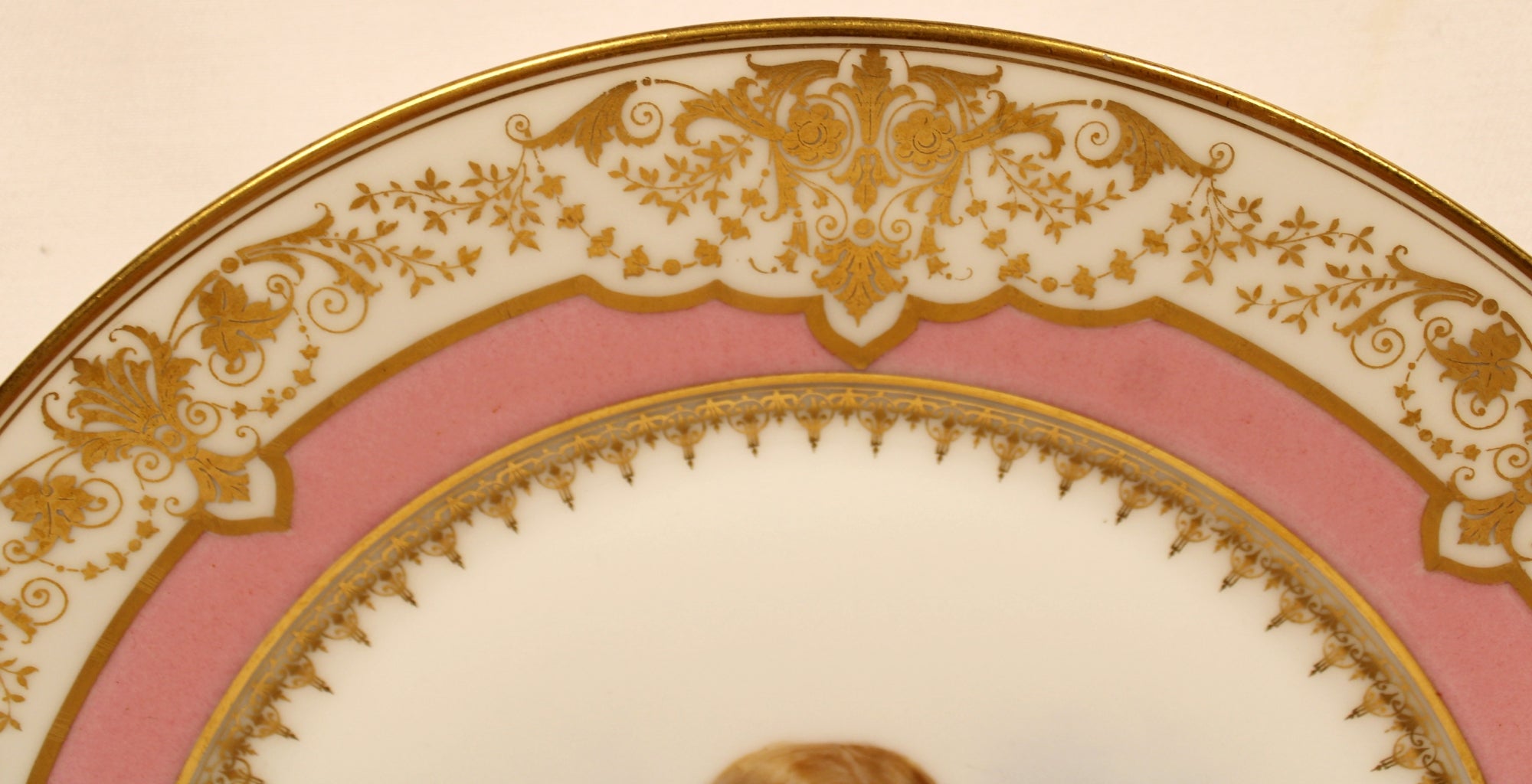 Decorative plate with gold intricate patterns on a pink background top rim