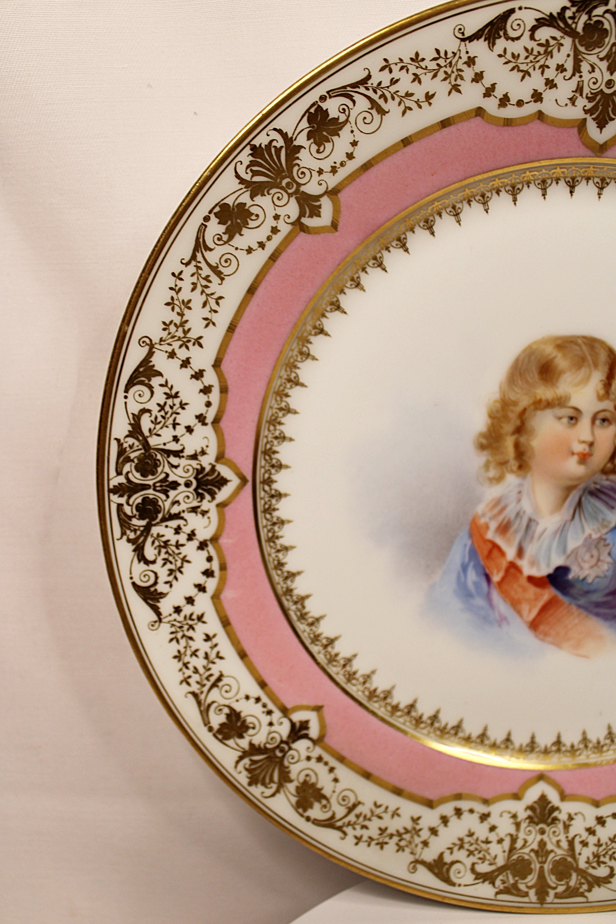 Decorative plate with a portrait of a child on a pink background left rim closeup