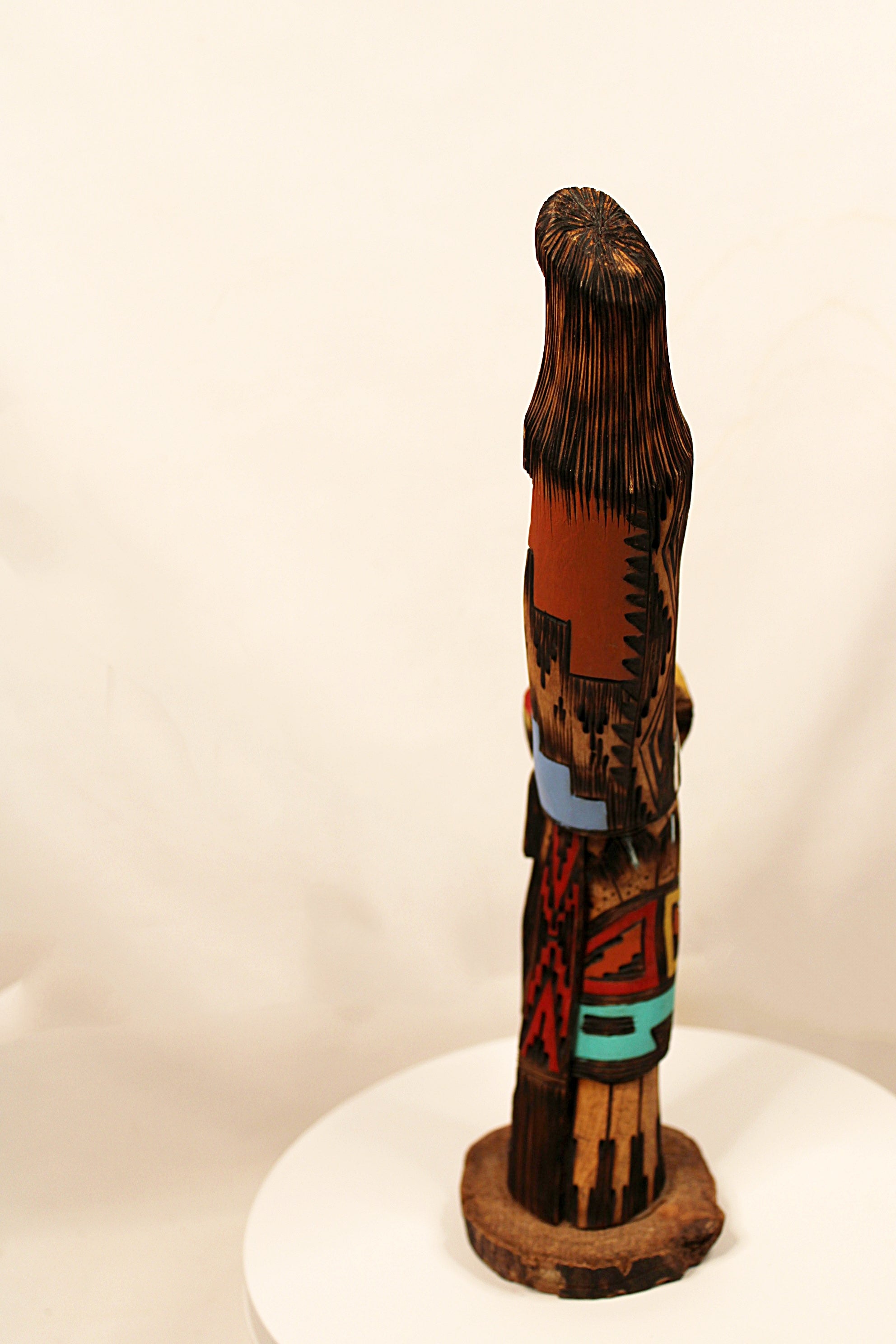 Decorative wooden sculpture with intricate patterns on a white pedestal against a beige background