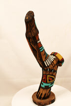 Wooden sculpture with colorful patterns on a white pedestal against a beige background