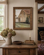 Framed painting of a barn on a wall above a wooden table with decorative items.