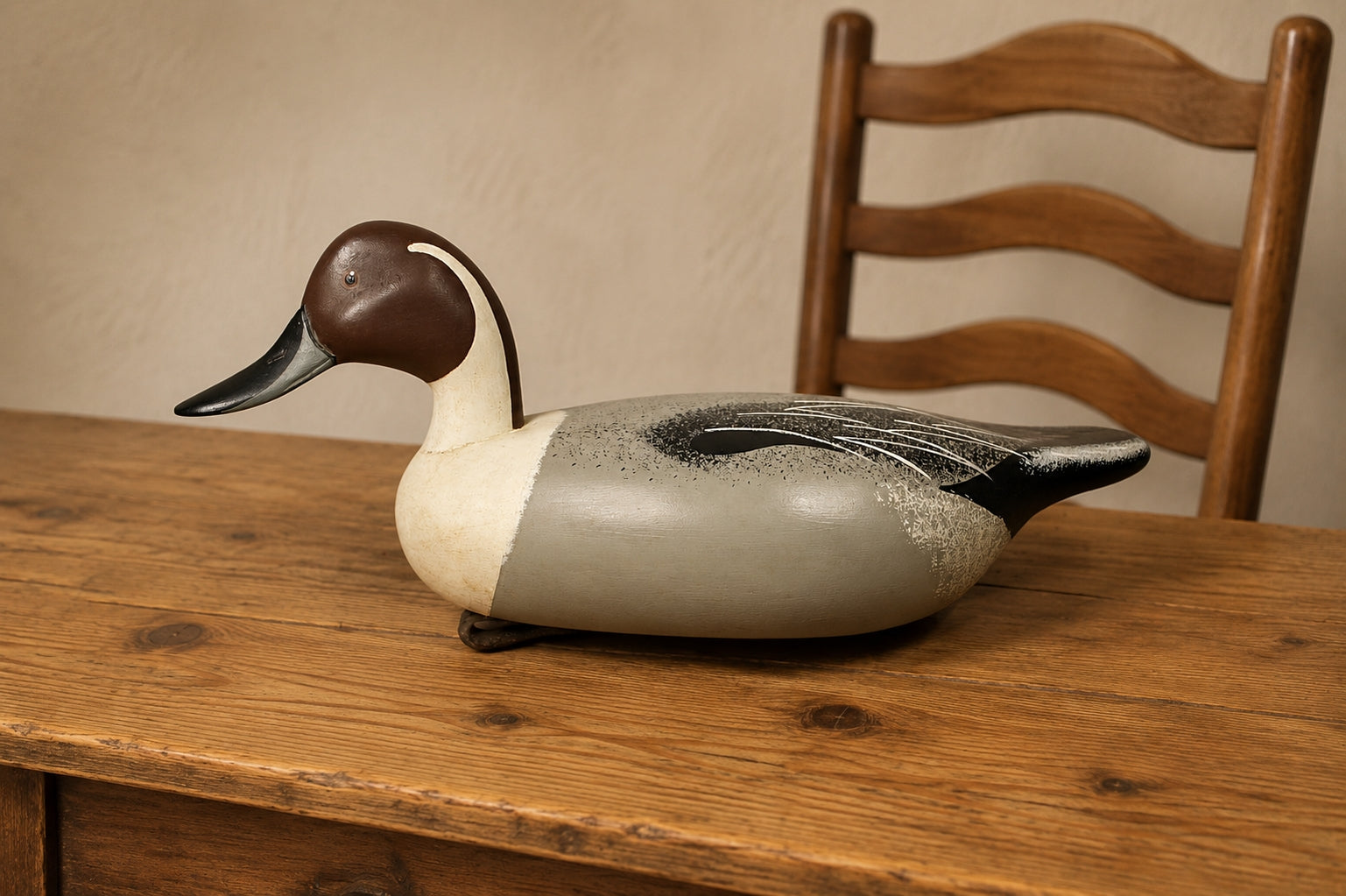 Decorative duck sculpture on a wooden table with a wooden chair in the background. Pintail Drake Duck Decoy Jim Burtis Maryland 1994
