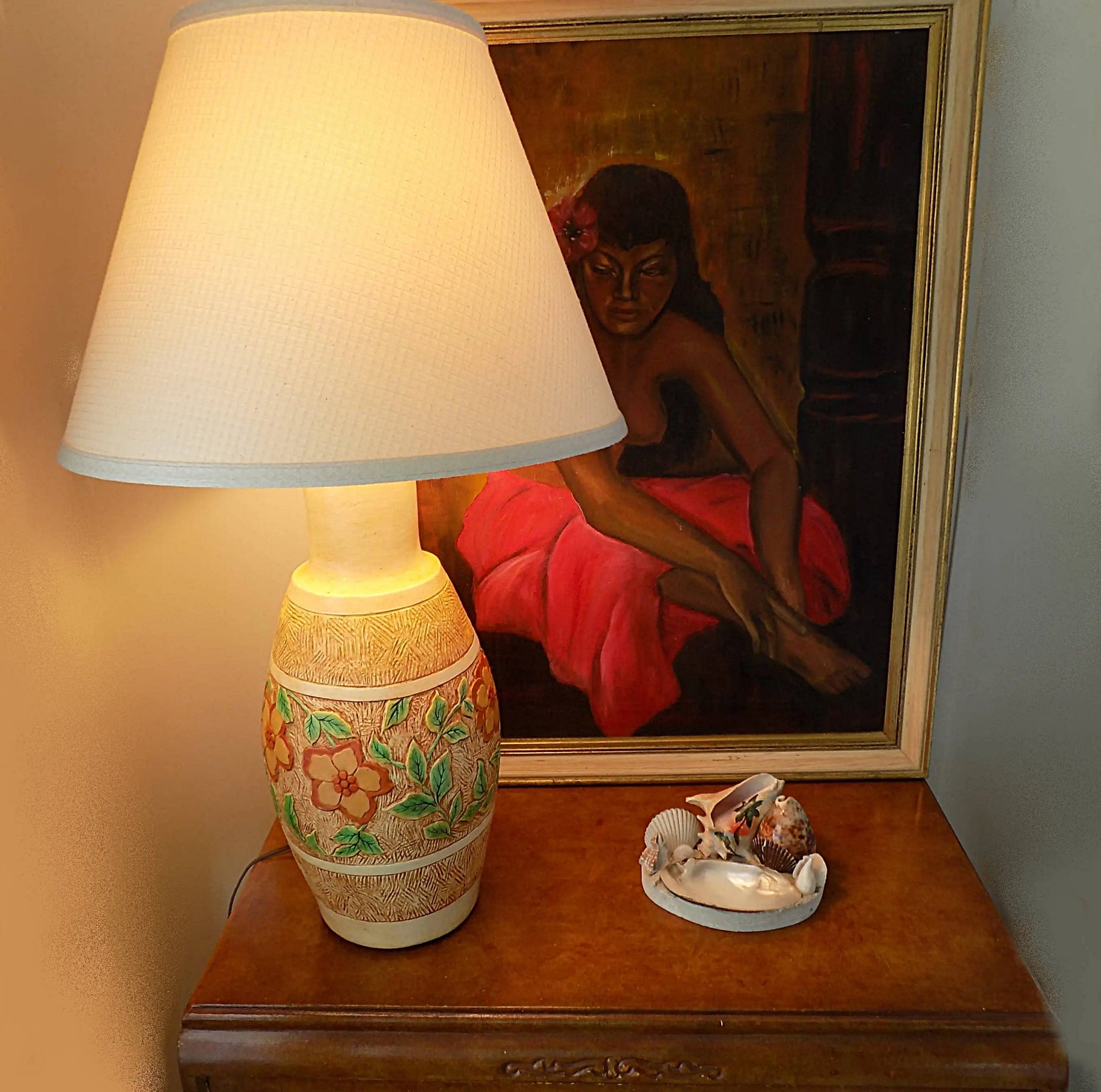 Decorative lamp on a table with a painting in the background and shell art dish in front